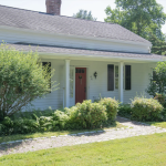 Front view of the historic colonial home at 44 Mountain Rd, Farmington, CT 06032, showcasing a well-maintained garden and a traditional red door under a shaded porch.